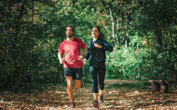 Ein Mann und eine Frau joggen durch einen Wald.