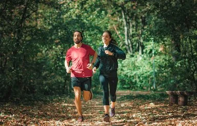 Ein Mann und eine Frau joggen durch einen Wald.