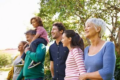 Eine Gruppe von fünf Personen unterschiedlichen Alters steht im Freien unter einem Baum, ein Kind sitzt auf den Schultern eines Mannes.