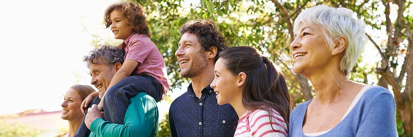 Eine Gruppe von fünf Personen unterschiedlichen Alters steht im Freien unter einem Baum, ein Kind sitzt auf den Schultern eines Mannes.