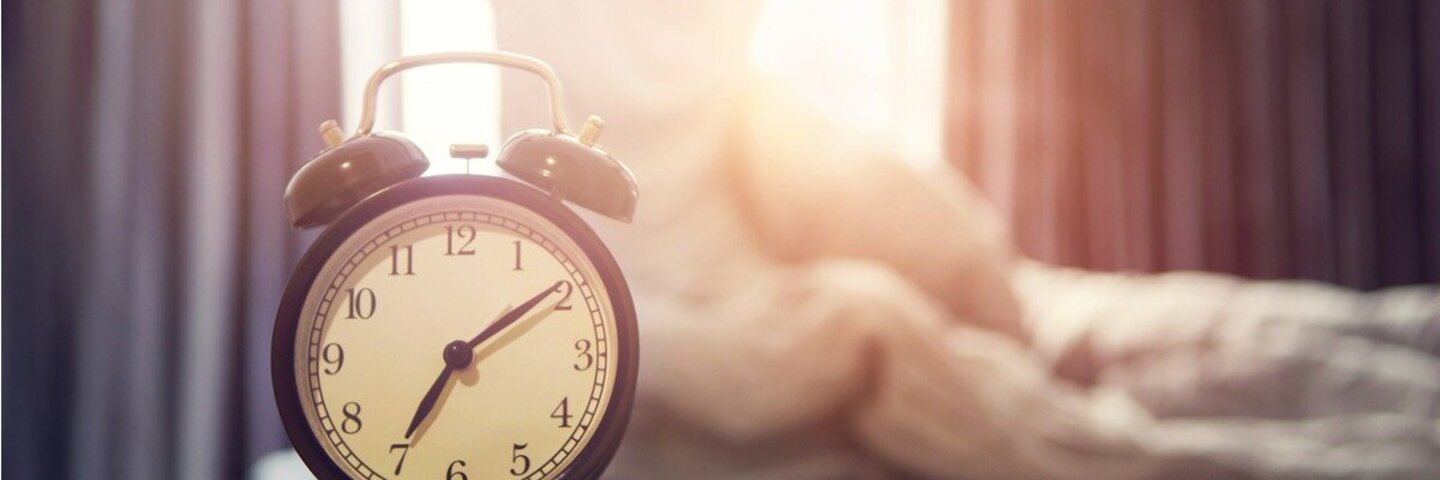 Eine Frau streckt sich am frühen Morgen gut gelaunt und dem Fenster zugewandt auf Ihrem Bett