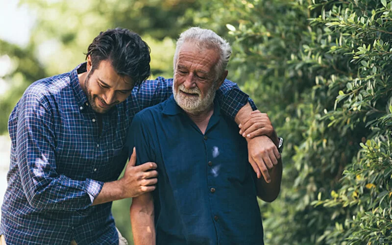 Ein Mann und sein Vater gehen Arm in Arm spazieren und sprechen über Sorgen.