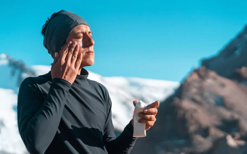 Ein Mann in den Bergen cremt sein Gesicht mit Sonnencreme ein.