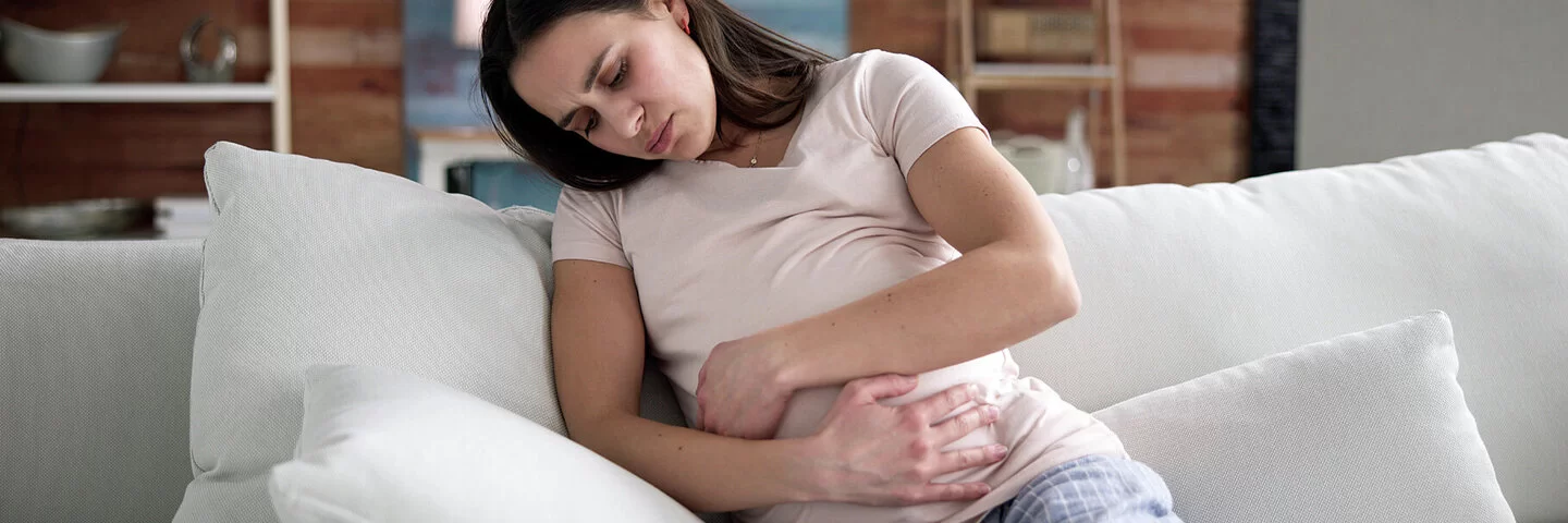 Eine Schwangere mit Verstopfungen sitzt auf dem Sofa und hält sich den Bauch.