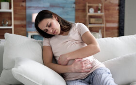 Eine Schwangere mit Verstopfungen sitzt auf dem Sofa und hält sich den Bauch.