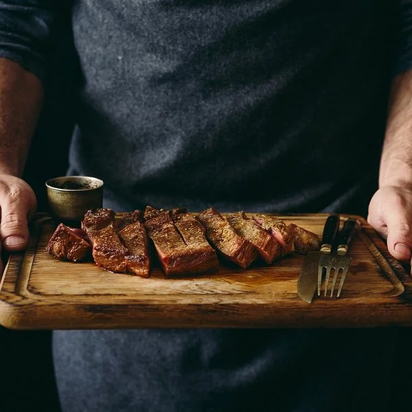 Ein Mann hält ein Schneidebrett mit einem gegrillten und in Scheiben geschnittenen Rindersteak.