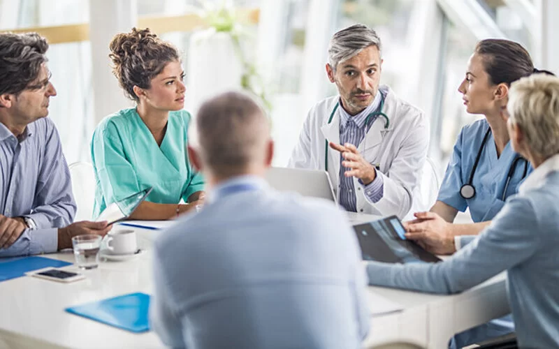 Ein Team aus Ärzten sitzt an einem Tisch und bespricht einen Fall von chronischen Schmerzen.