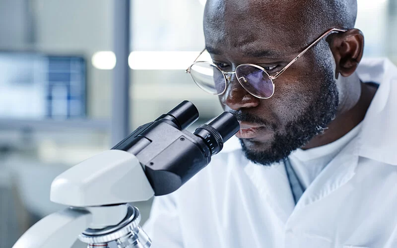 Ein Laborarzt betrachtet durch ein Mikroskop eine Gewebeprobe.