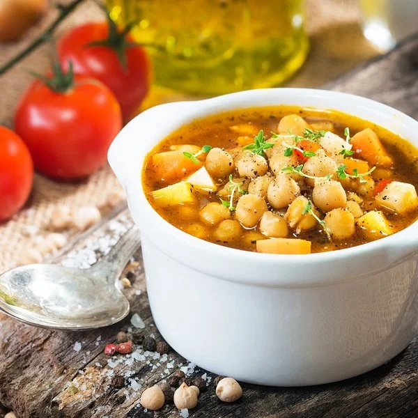 Ein warmer Kichererbsen-Eintopf steht in einem kleinen Suppenschälchen auf einem Tisch.