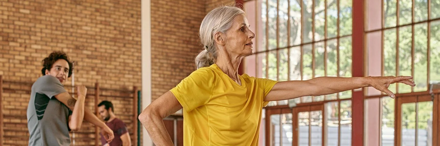 Mehrere Personen in Sportkleidung machen Übungen in einer Sporthalle. Die AOK unterstützt sie in Sachen Bewegung.