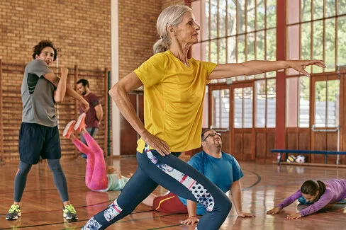 Mehrere Personen in Sportkleidung machen Übungen in einer Sporthalle. Die AOK unterstützt sie in Sachen Bewegung.