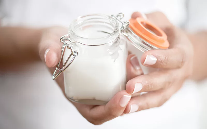 Eine Frau hält ein wiederverschließbares Glas in der Hand, in welches sie ihre selbstgemachte Handcreme abgefüllt hat.