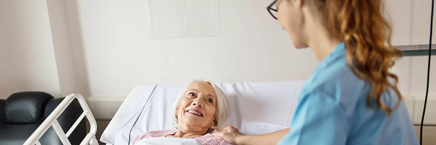 Eine Krankenschwester legt beide Hände auf den Körper einer älteren Patientin. Zusatzversicherungen der AOK bieten beim Krankenhausaufenthalt größten Komfort.