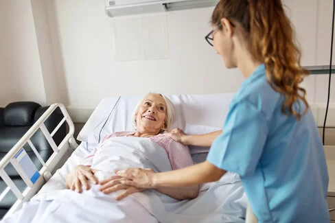 Eine Krankenschwester legt beide Hände auf den Körper einer älteren Patientin. Zusatzversicherungen der AOK bieten beim Krankenhausaufenthalt größten Komfort.