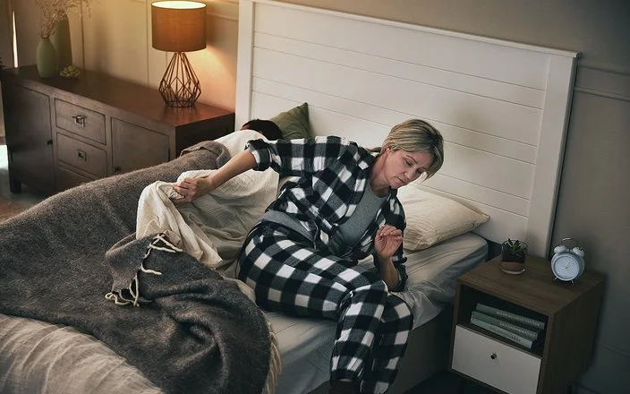 Eine Frau steht im Schlafanzug aus ihrem Bett auf.