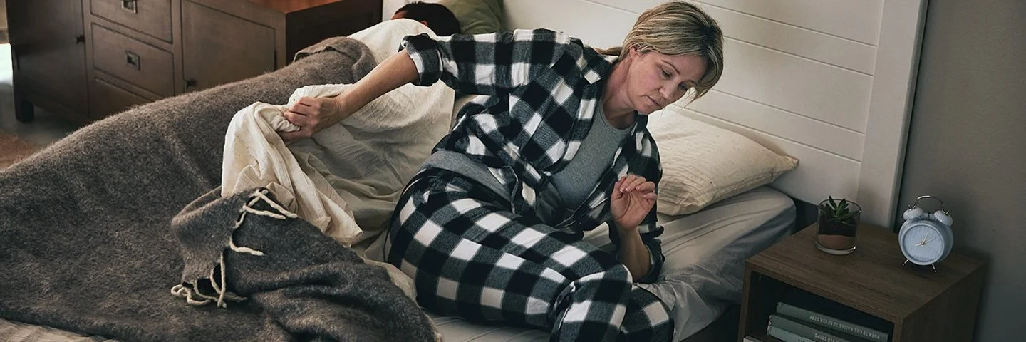 Eine Frau steht im Schlafanzug aus ihrem Bett auf.