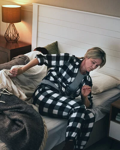 Eine Frau steht im Schlafanzug aus ihrem Bett auf.