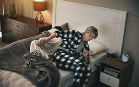 Eine Frau steht im Schlafanzug aus ihrem Bett auf.