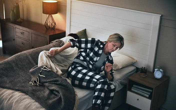 Eine Frau steht im Schlafanzug aus ihrem Bett auf.