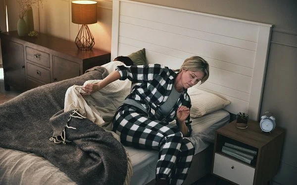 Eine Frau steht im Schlafanzug aus ihrem Bett auf.