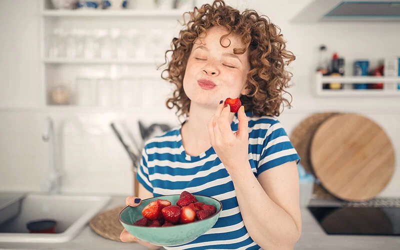 Eine Frau steht in der Küche und isst genüßlich Erdbeeren aus einer Schüssel.