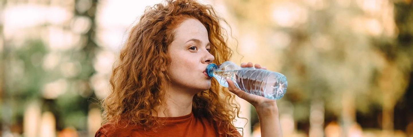 Frau mit lockigem Haar trinkt aus einer Wasserflasche im Freien.