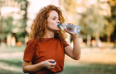 Frau mit lockigem Haar trinkt aus einer Wasserflasche im Freien.