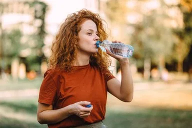 Frau mit lockigem Haar trinkt aus einer Wasserflasche im Freien.