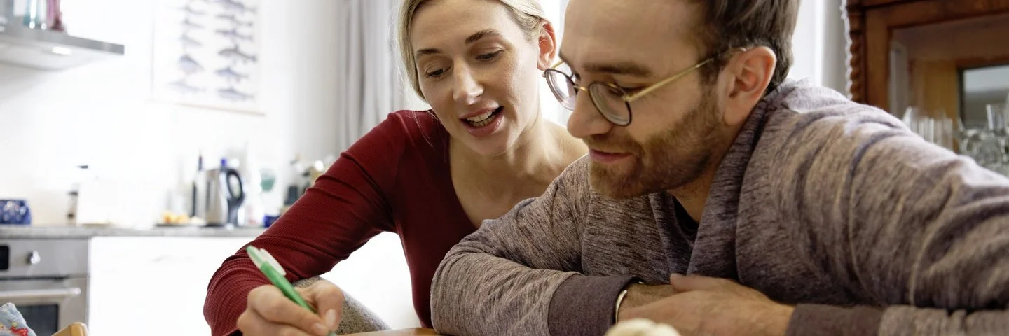 Frau und Mann sitzen an einem Tisch zusammen und füllen mit einem Stift einen Antrag aus.