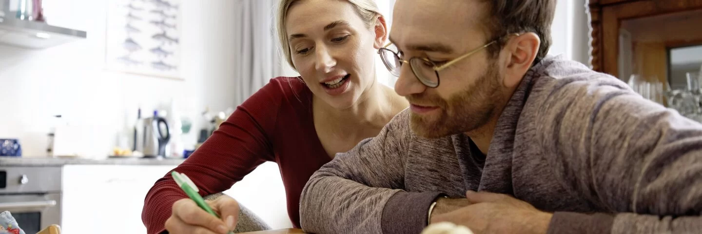 Frau und Mann sitzen an einem Tisch zusammen und füllen mit einem Stift einen Antrag aus.