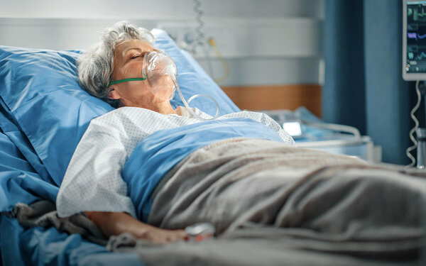 Eine Frau, die an einer Lungenembolie erkrankt ist, liegt mit Beatmungsmaske in einem Krankenhausbett.
