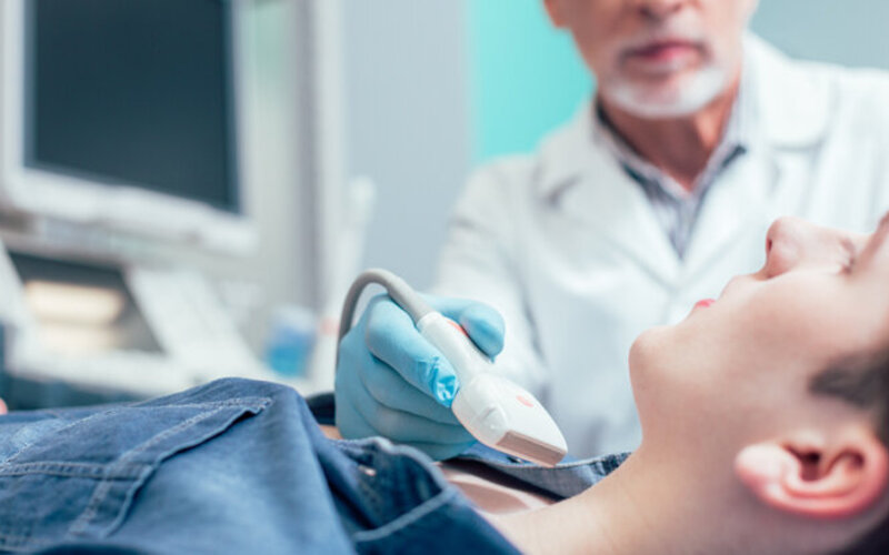 Ein Arzt führt eine Ultraschalluntersuchung der Schilddrüse bei einer Frau durch.