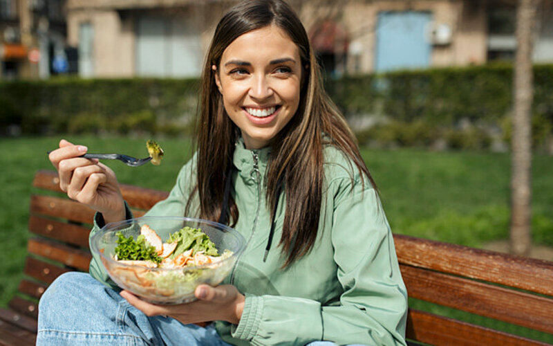 Eine Frau isst in einem Park ihr vorbereitetes und mitgebrachtes Essen.
