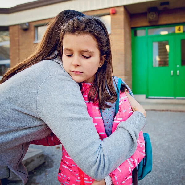 Mädchen hat Angst zur Schule zu gehen und umarmt ihre Mutter traurig.