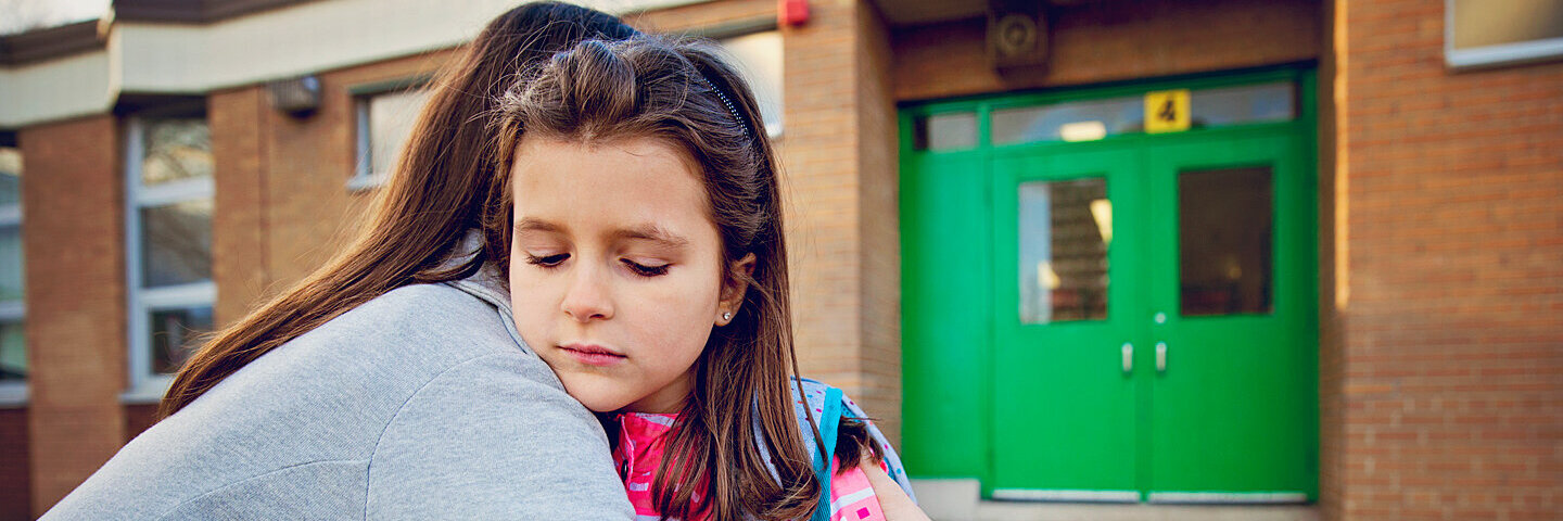 Mädchen hat Angst zur Schule zu gehen und umarmt ihre Mutter traurig.