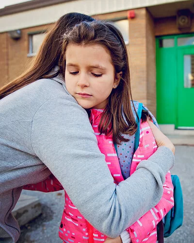 Mädchen hat Angst zur Schule zu gehen und umarmt ihre Mutter traurig.