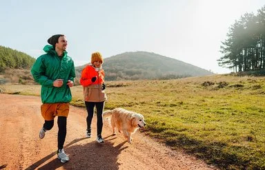 Ein Mann und eine Frau joggen gemeinsam mit einem Hund in der Natur.
