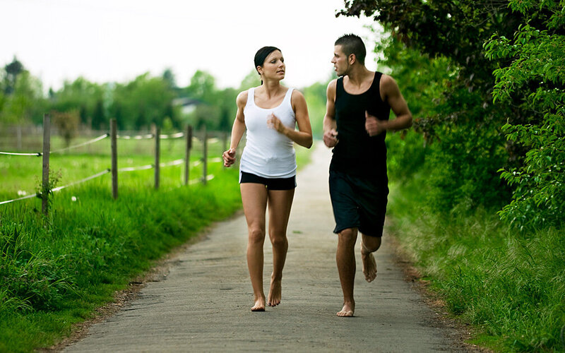 Ein junges Paar joggt barfuß auf einem asphaltierten Feldweg.