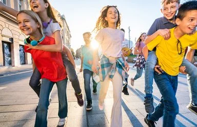 Eine Gruppe fröhlicher Kinder läuft auf einer sonnigen Straße in Richtung Kamera.