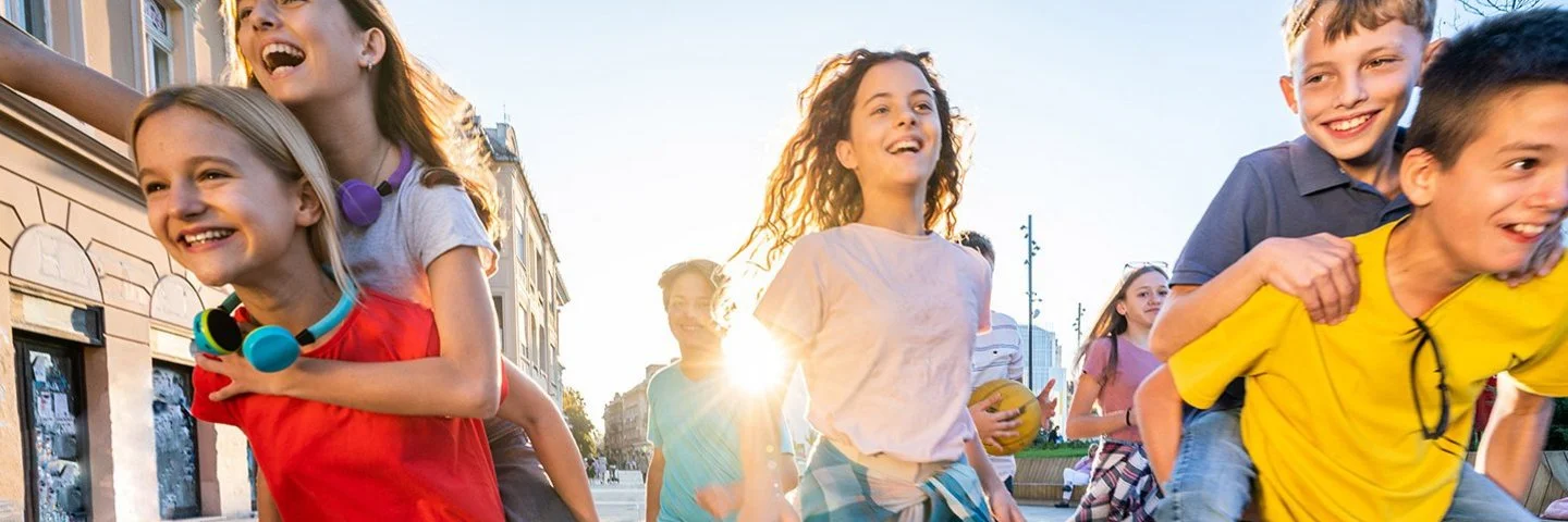 Eine Gruppe fröhlicher Kinder läuft auf einer sonnigen Straße in Richtung Kamera.
