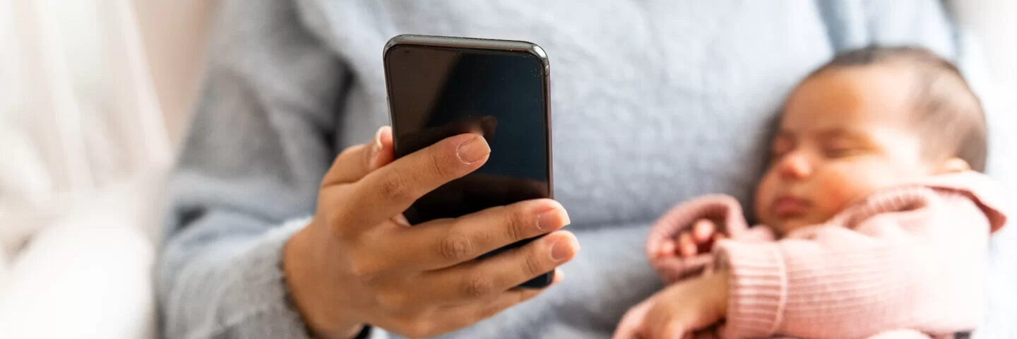 Eine Frau mit einem Baby am Arm telefoniert. Die AOK berät Eltern telefonisch mit wichtigen Informationen zur Gesundheit ihrer Kinder.