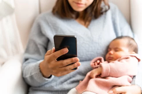 Eine Frau mit einem Baby am Arm telefoniert. Die AOK berät Eltern telefonisch mit wichtigen Informationen zur Gesundheit ihrer Kinder.
