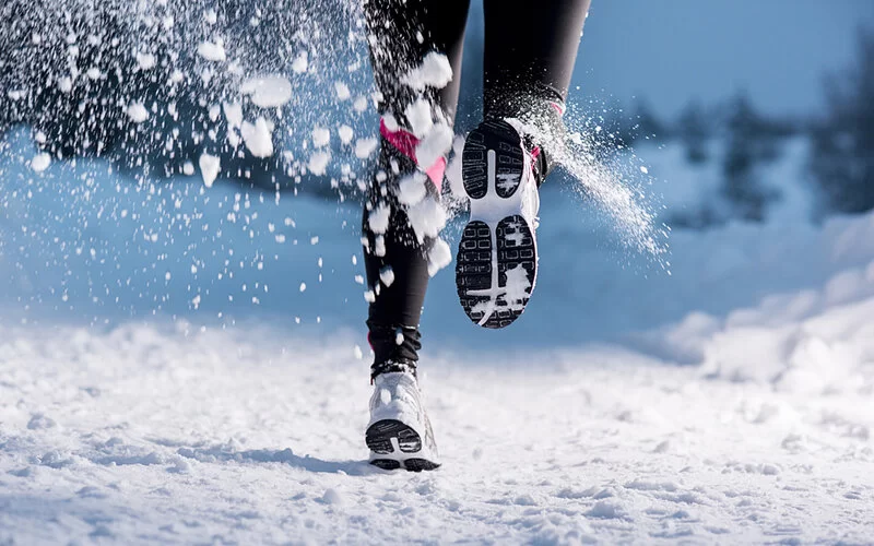 Eine Person wirbelt Schnee beim Joggen im Winter auf.