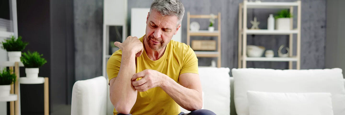 Mann sitzt auf dem Sofa und kratzt sich den Unterarm.