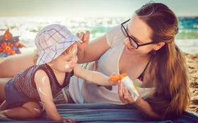 Mutter cremt ihr Baby für richtigen Sonnenschutz mit Sonnencreme ein.