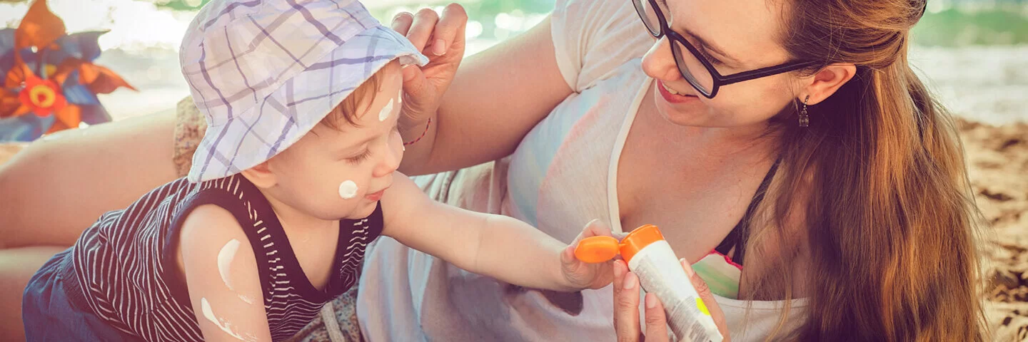 Mutter cremt ihr Baby für richtigen Sonnenschutz mit Sonnencreme ein.
