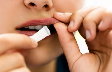 Eine junge Person steckt sich ein weißes Snus-Beutelchen unter die Oberlippe.