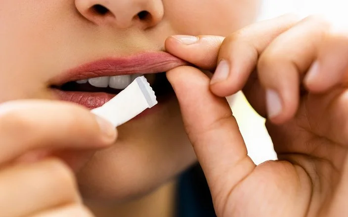 Eine junge Person steckt sich ein weißes Snus-Beutelchen unter die Oberlippe.