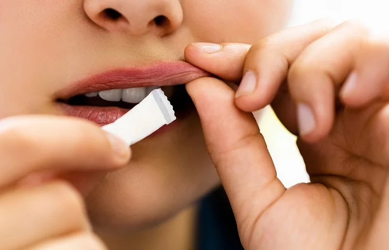 Eine junge Person steckt sich ein weißes Snus-Beutelchen unter die Oberlippe.