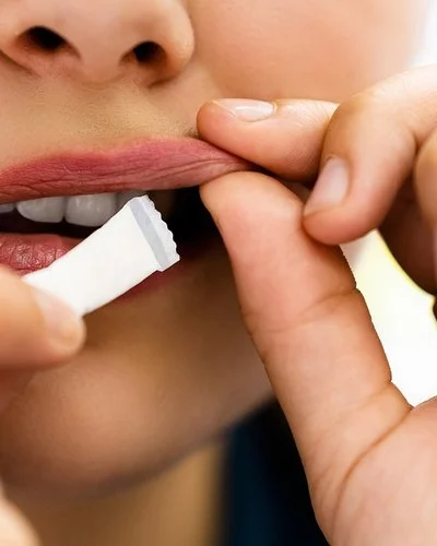 Eine junge Person steckt sich ein weißes Snus-Beutelchen unter die Oberlippe.